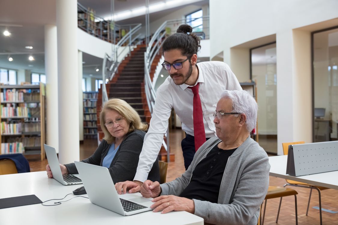 A mentor helping adults learn to use laptops